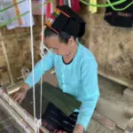 Artisan weaving dark fabric on a traditional wooden loom