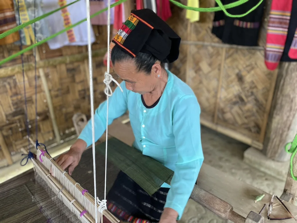 Artisan weaving dark fabric on a traditional wooden loom
